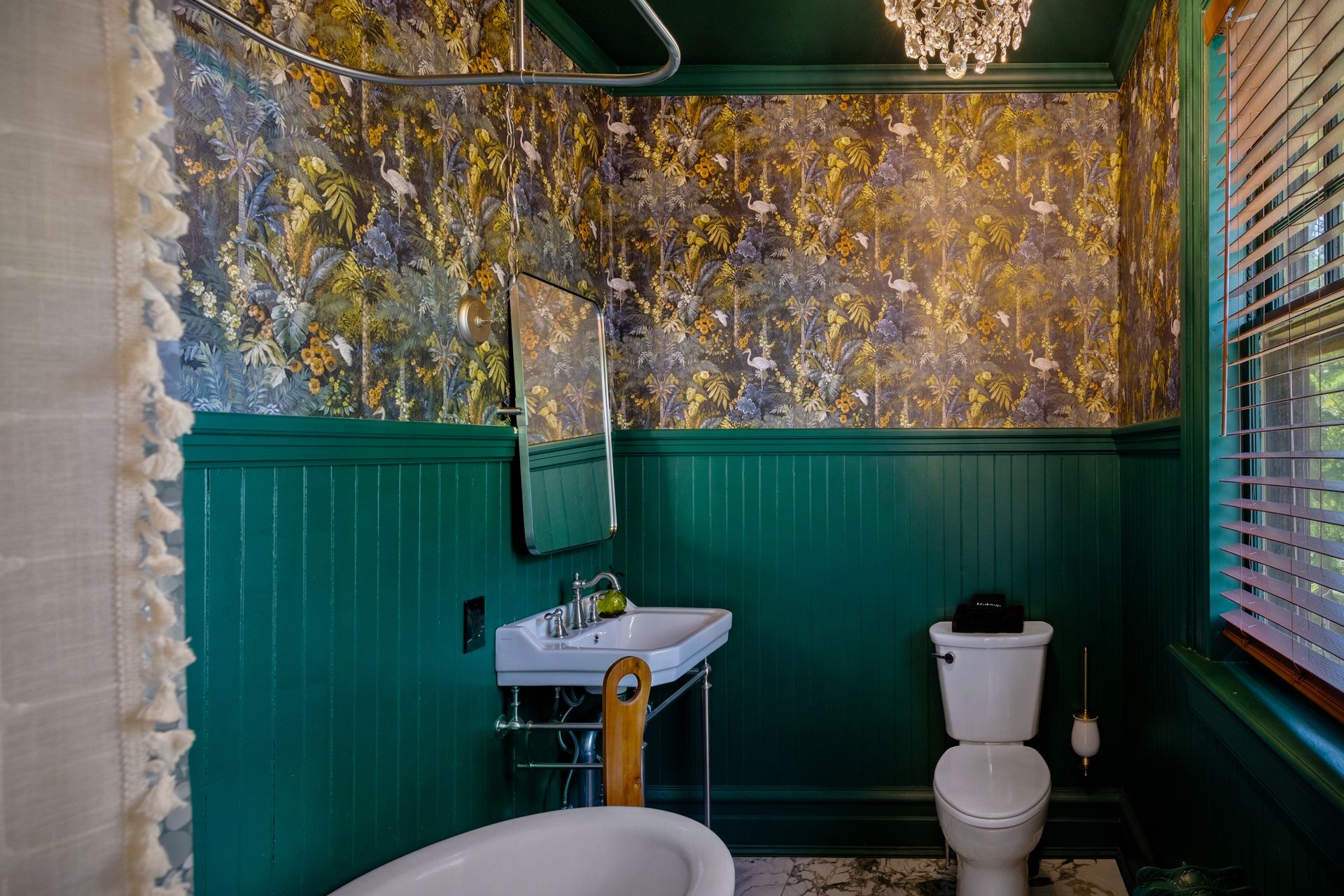 Green bathroom with botanical wallpaper and original clawfoot tub with aged patina